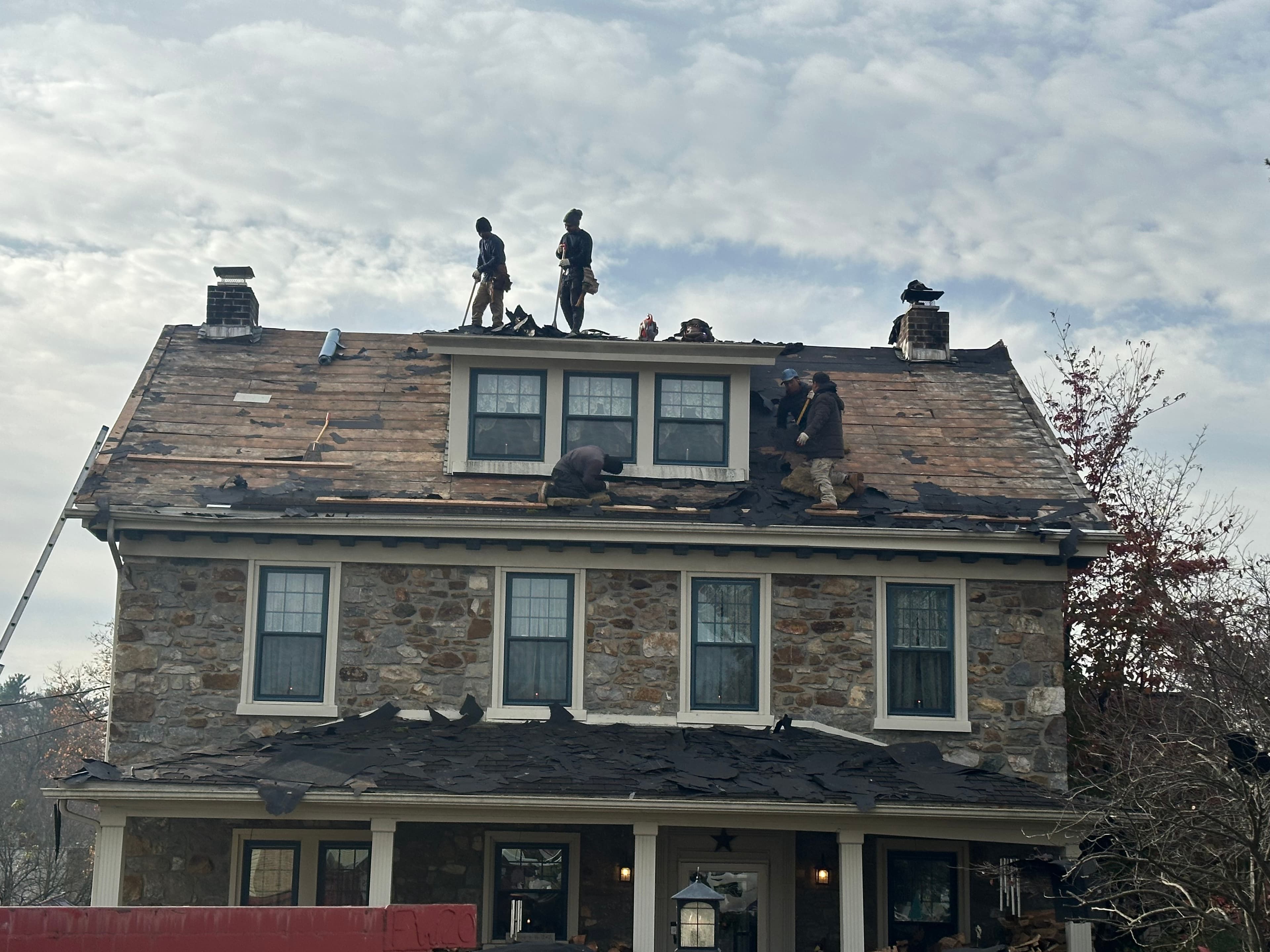 E&K roofing crew performing a full tear-off on a stone colonial, stripping old shingles down to the deck