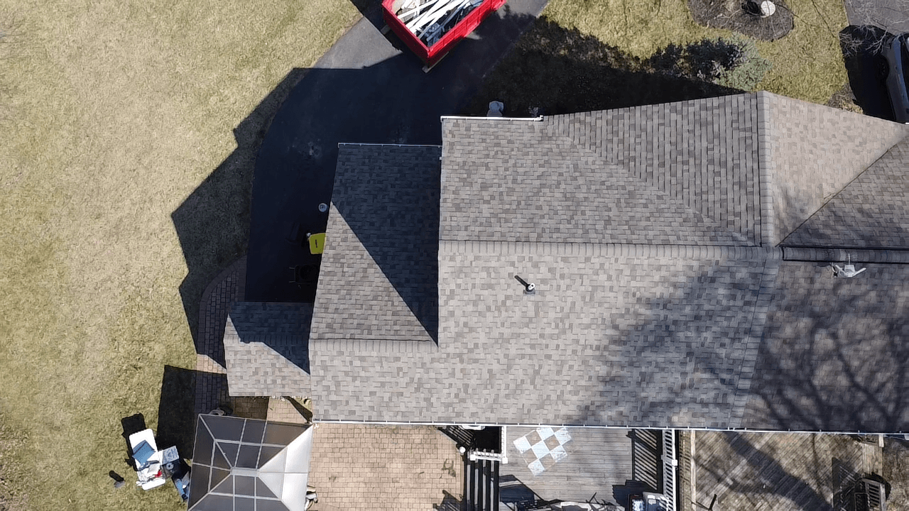 Overhead drone view of a finished shingle roof replacement, showing clean ridge lines above a rear patio