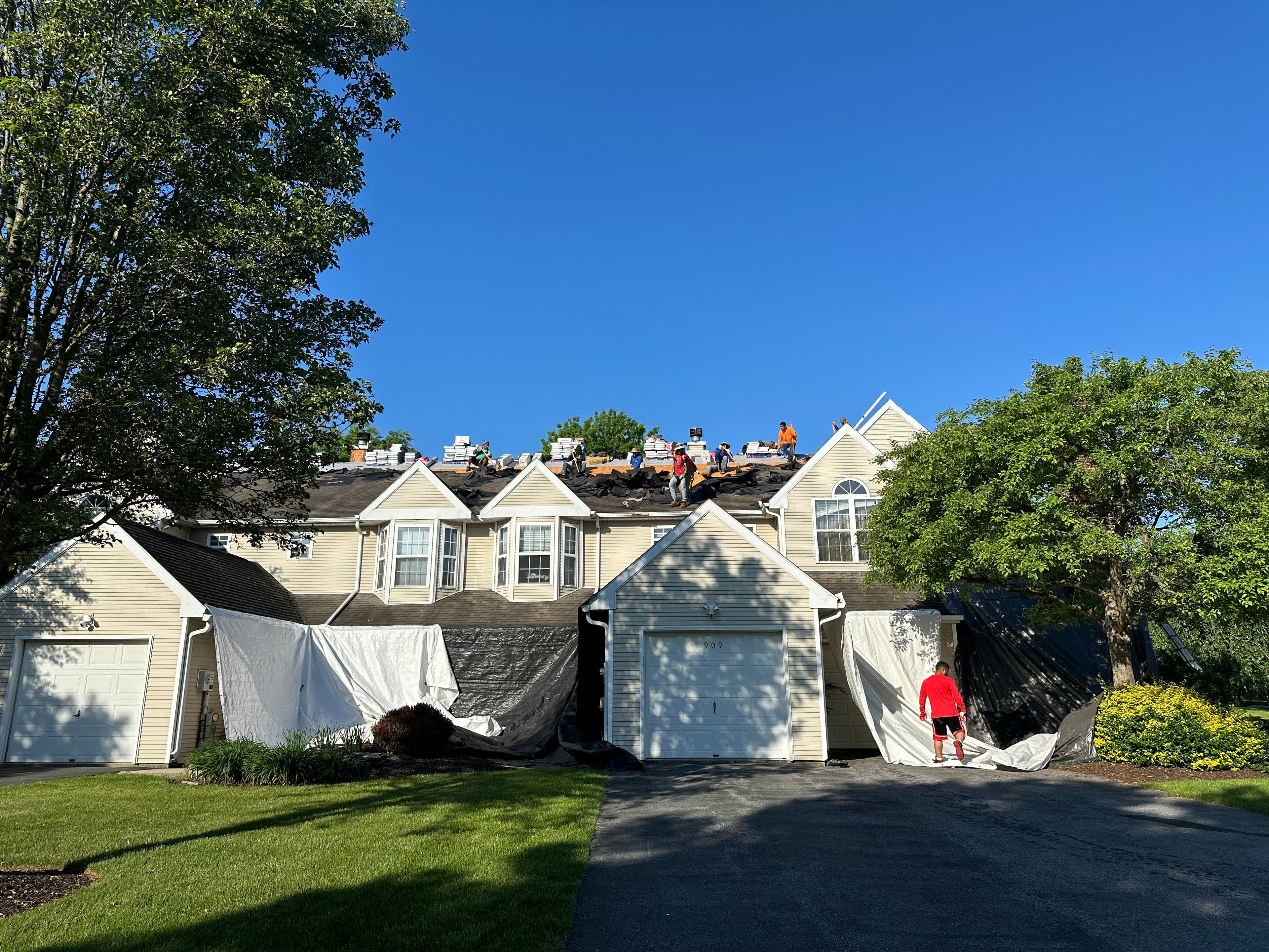 E&K crew mid-roof-replacement on a row of townhomes, with tarps protecting the siding and landscaping below